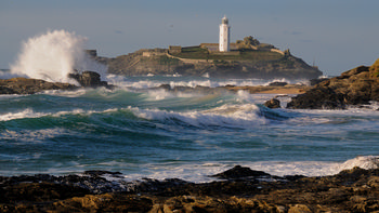 Godrevy waves This landscape photograph captures the waves of Godrevy surging along the rocky coast in Cornwall, United Kingdom. The image was taken on a November afternoon during autumn, as evidenced by the cool lighting and active sea conditions characteristic of the season. Prominently visible is the Godrevy Lighthouse, a well-known landmark standing on the island and overlooking the natural coastline. The scene highlights the power of nature as waves crash against the rocks, sending plumes of sea spray into the air. The combination of the turbulent sea, the rugged coastline, and the white lighthouse creates a dynamic representation of the United Kingdom’s coastal environment.